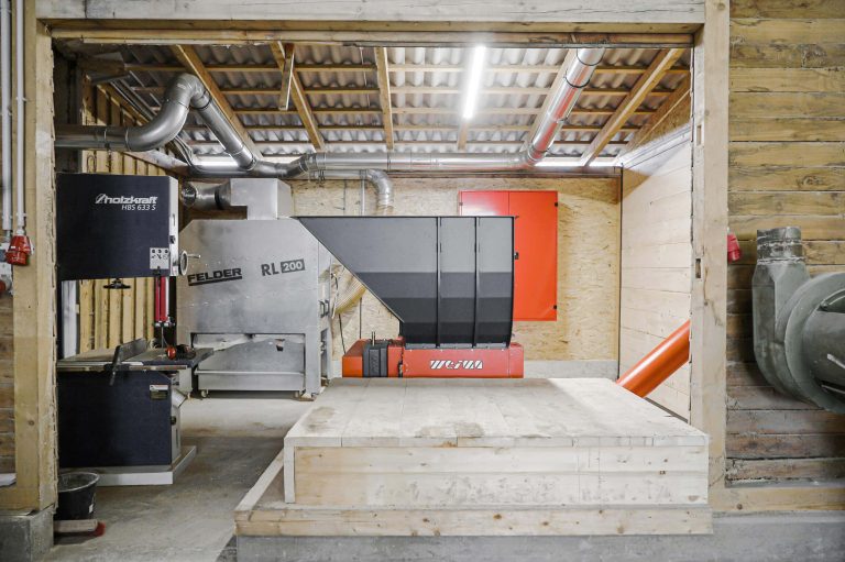 an orange single-shaft shredder sits in front of wood waste in a woodworking shop