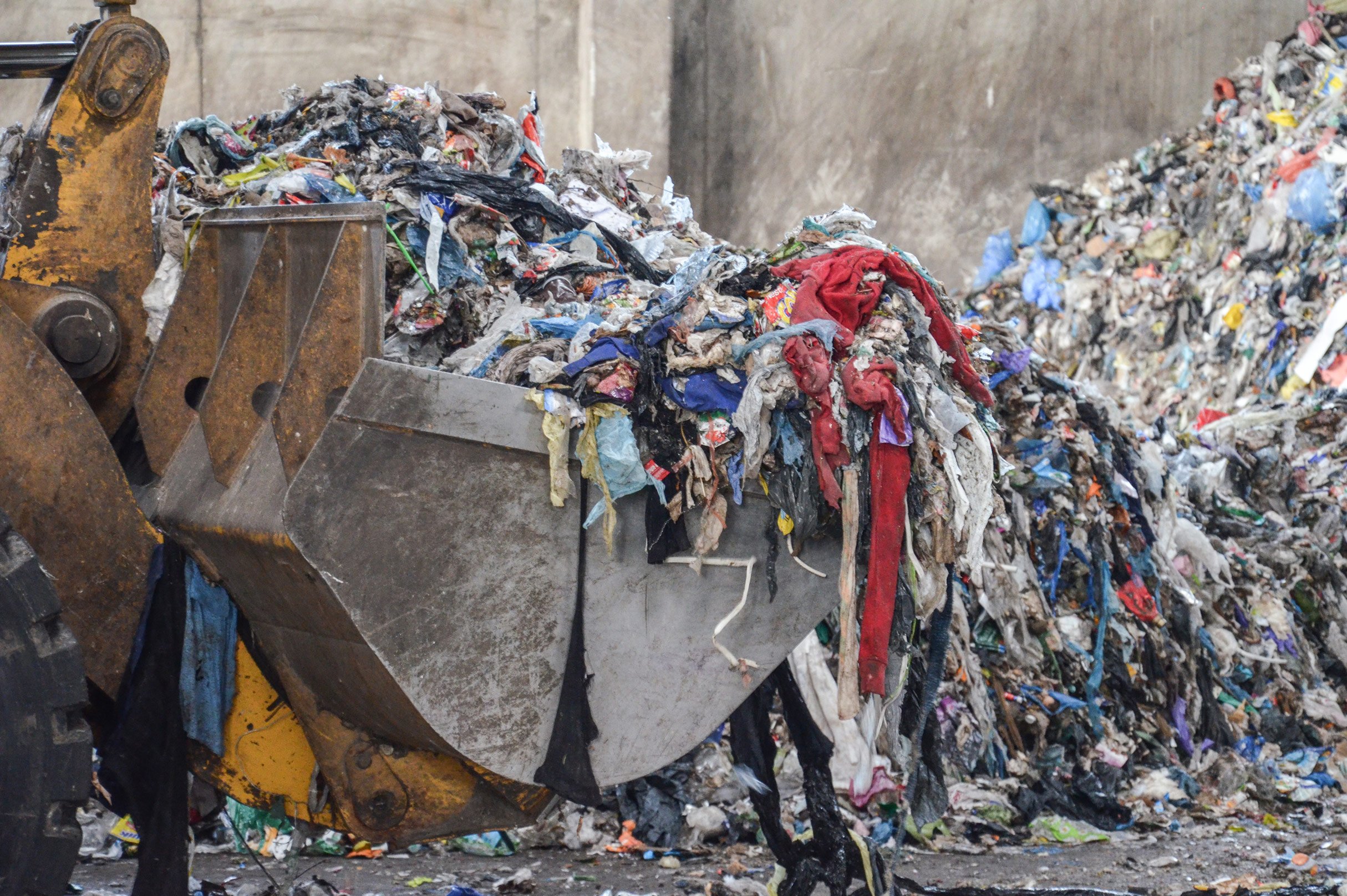 a pile of municipal garbage is scooped by a large piece of machinery