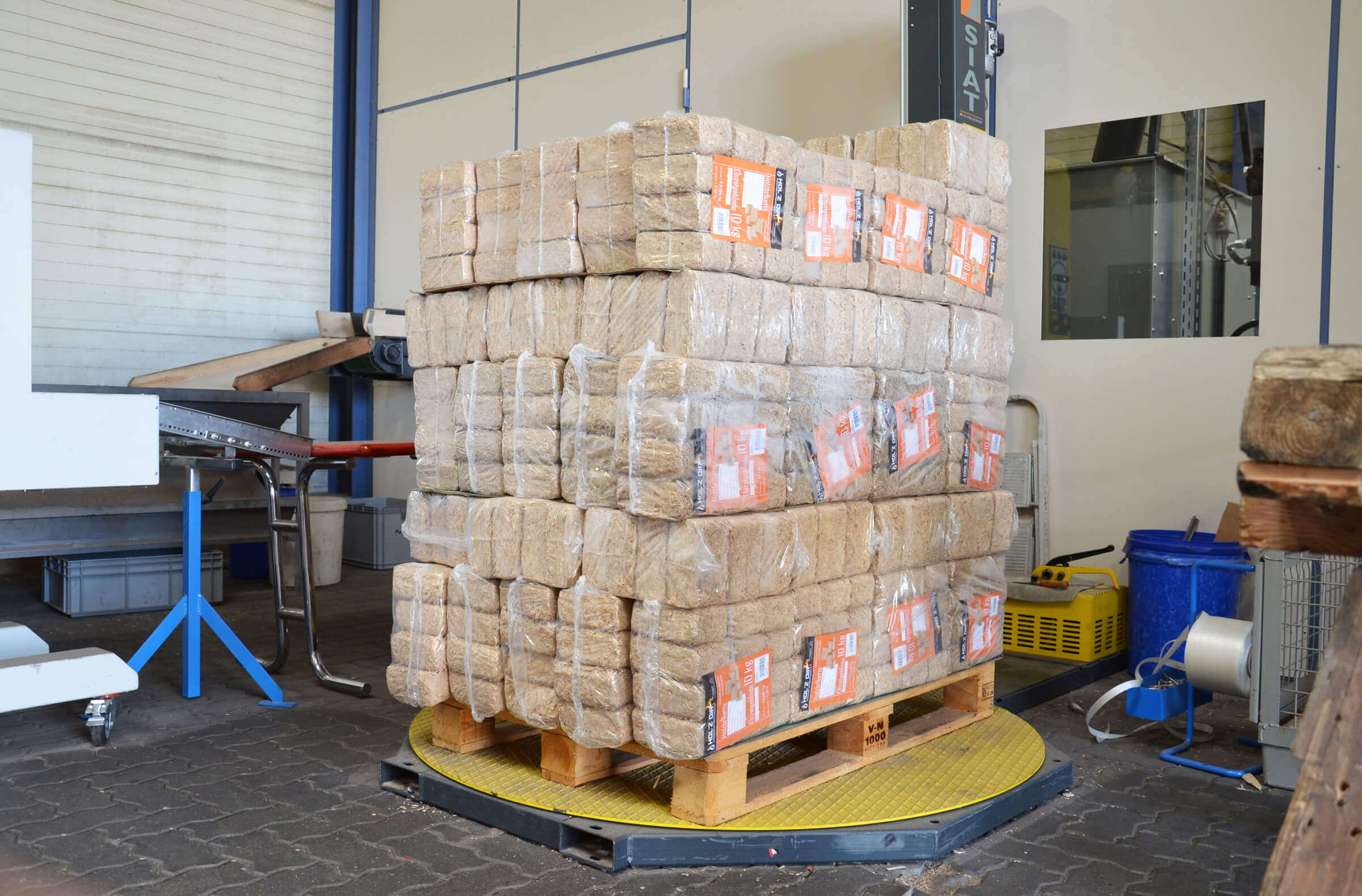 bereits abgepackte Holzbriketts werden auf einer Palette gestapelt und verwogen.