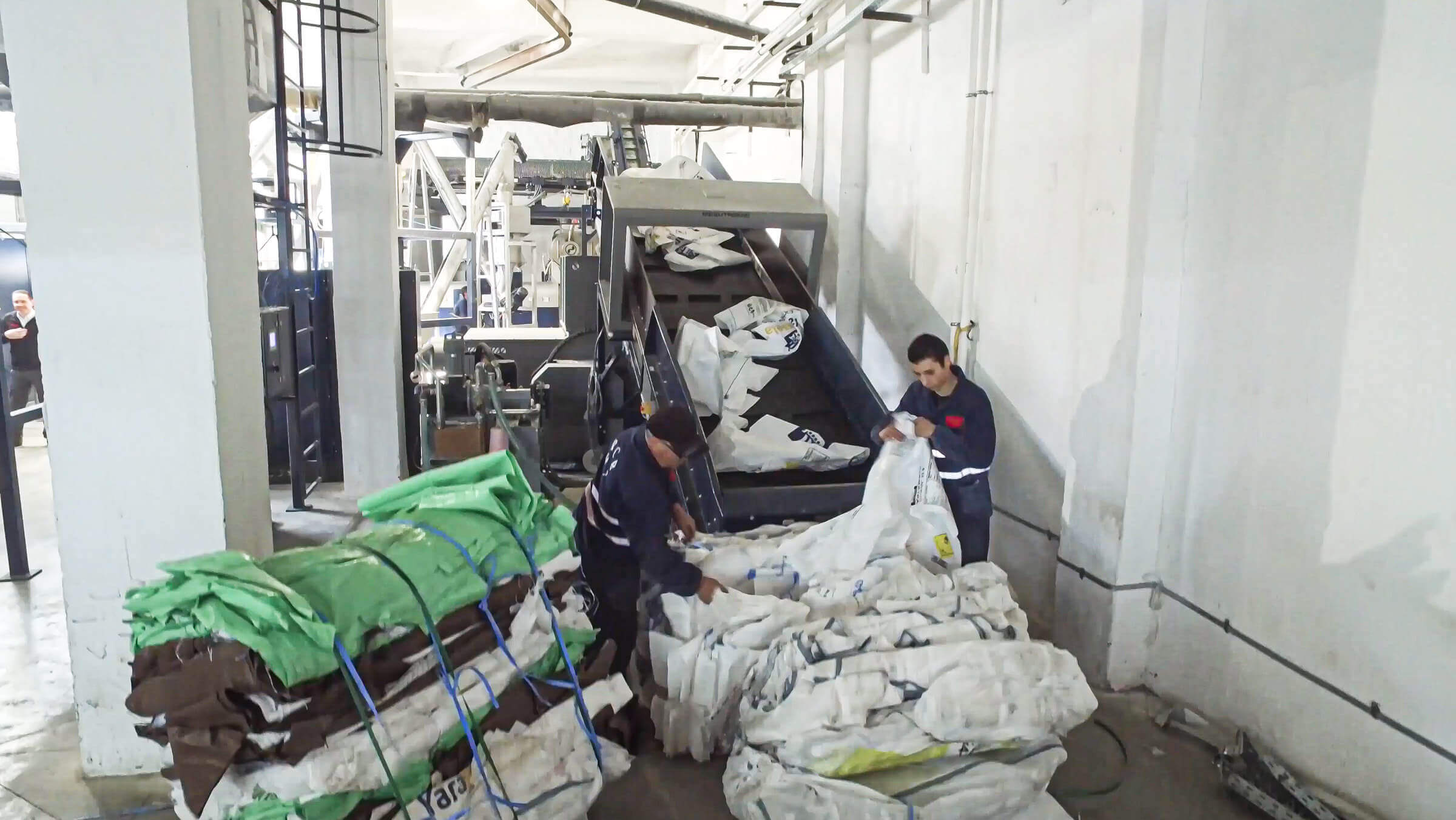 Mitarbeitende befördern mittels Fließband Plastiksäcke und Folien in den Schredder WLK1500