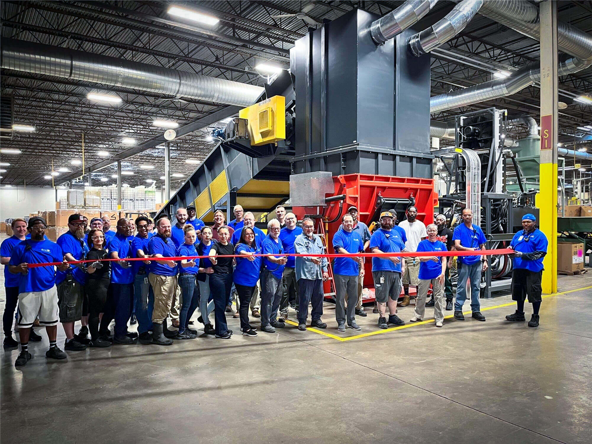 Viele Mitarbeiter mit blauen Shirts stehen vor einem großen WEIMA shhredder und zerschneiden ein rotes band