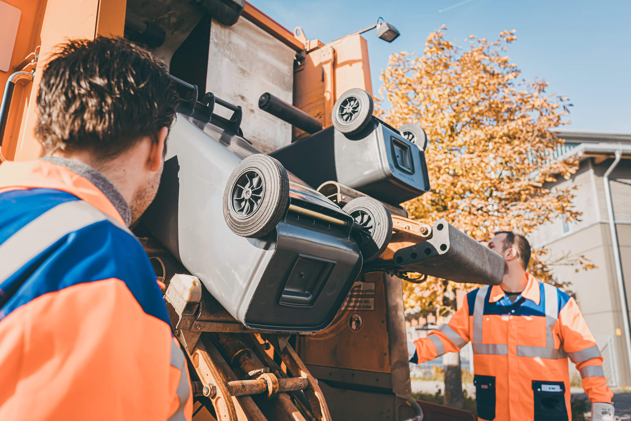 two men collecting household waste by emptying containers