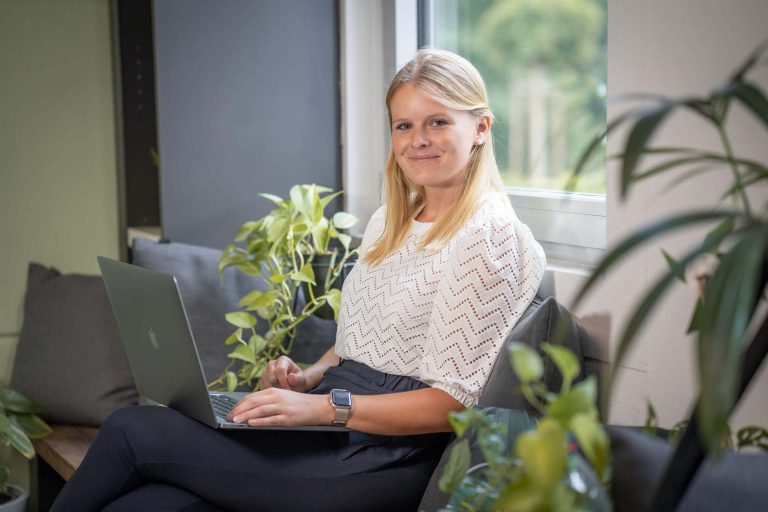 women with laptop sitting in front of a window smiling to camera