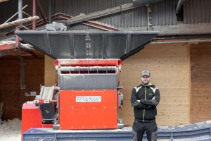 Eine rote WEIMA S7.15 steht vor einem Gebäude. Daneben steht ein Mitarbeiter der Firma und schaut in die Kamera.