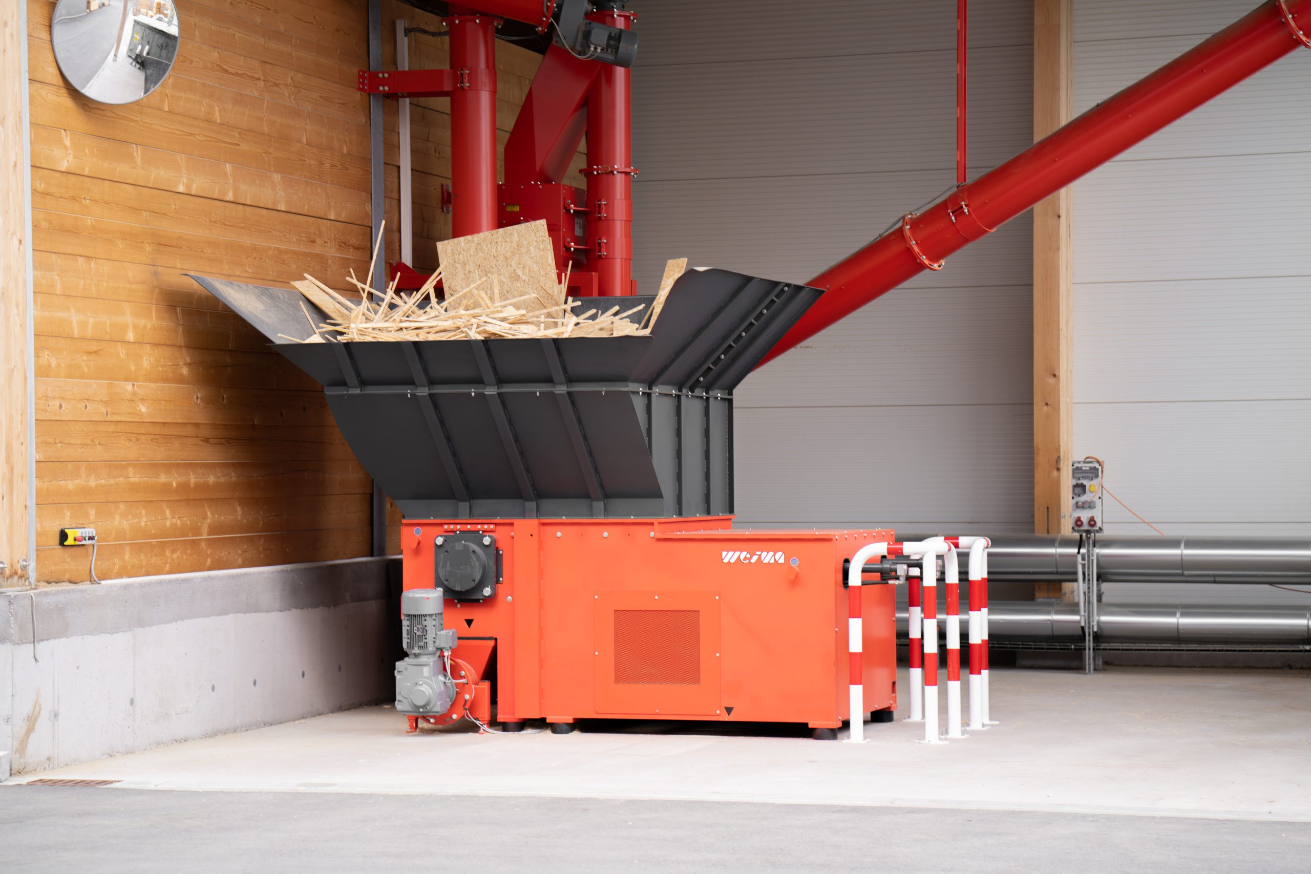 The WLK 1500 single-shaft shredder from WEIMA stands in front of a building. In the background is the associated control cabinet and the transport system consisting of screw conveyors and spirals.