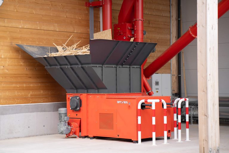 The WLK 1500 single-shaft shredder from WEIMA stands in front of a building. In the background is the associated control cabinet and the transport system consisting of screw conveyors and spirals.