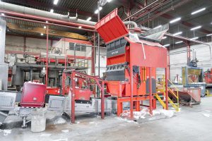 Orange-roter Shredder von WEIMA in Bildmitte, links daneben ein Austragsförderband, in einer industriellen Halle umgeben von Recycling-Anlagentechnik