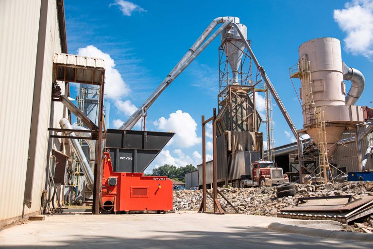 Orangener WEIMA Holzschredder im Freien, verbunden mit Absaugrohren zu einer weiteren Halle