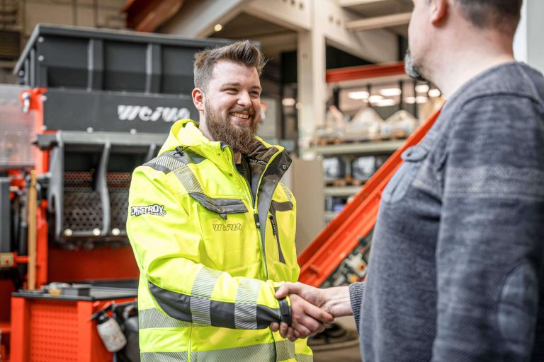 WEIMA service technician with yellow jacket greeting a customer in front of a shredding machine
