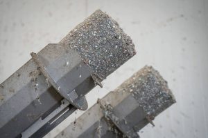 Entwässerte und komprimierte graue Klumpen aus Kunststoff Feinanteilen auf den Austragsrohren einer WEIMA C.200 Duo