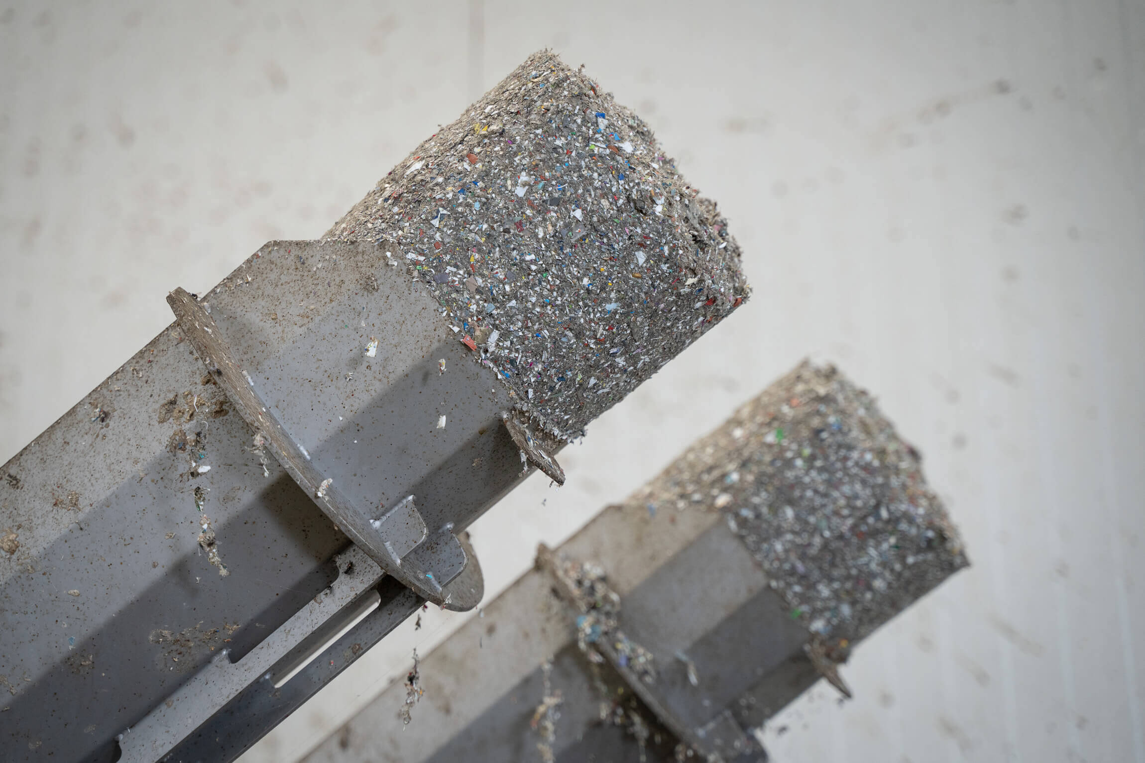 Dewatered and compressed gray lumps of plastic fines on the discharge pipes of a WEIMA C.200 Duo