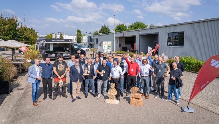 A group of smiling men in front of a company building.