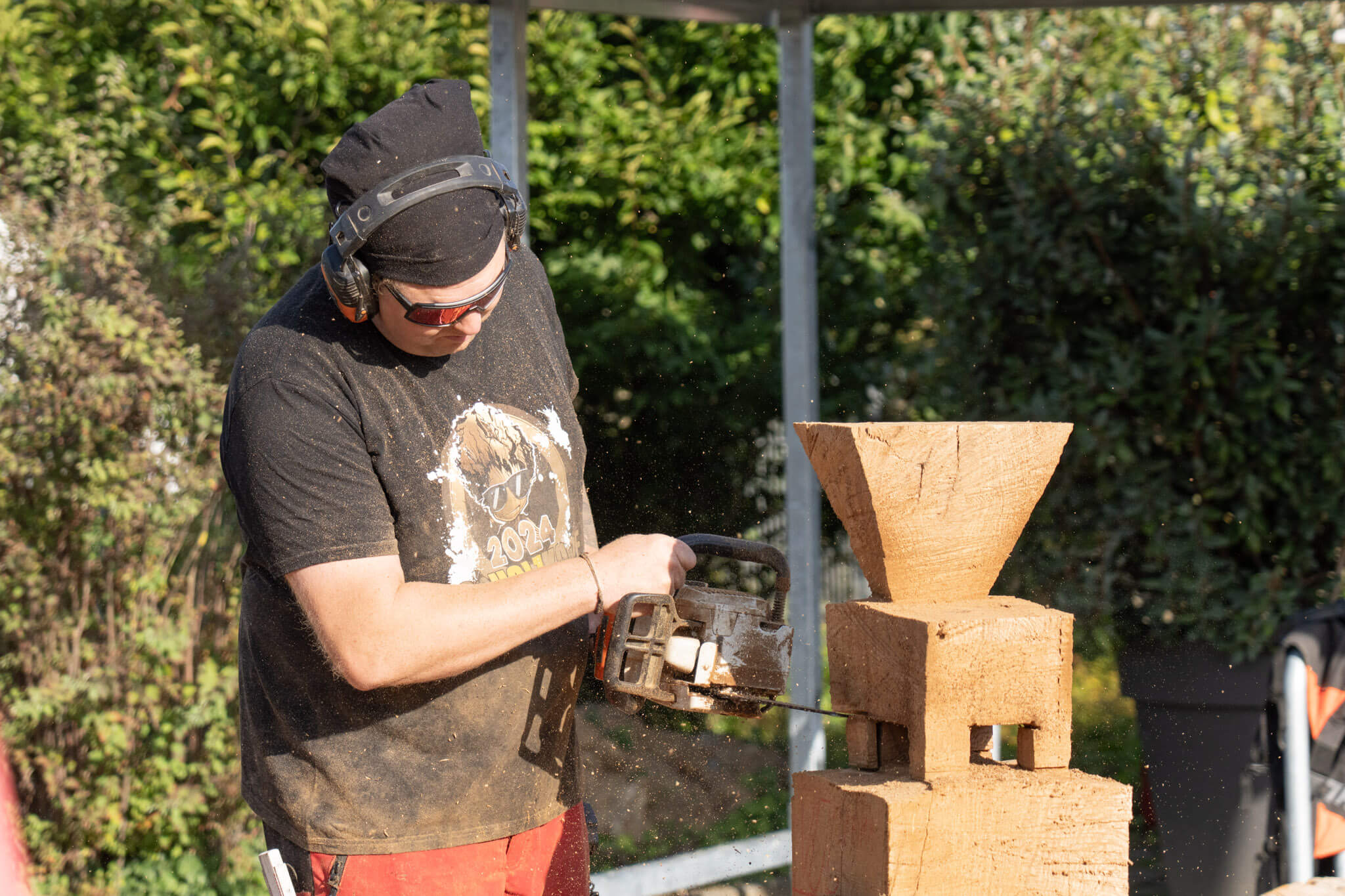 A man carves a WEIMA shredder out of a block of wood with a chainsaw