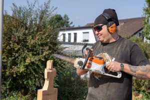 A man carves a figure out of a block of wood with a chainsaw