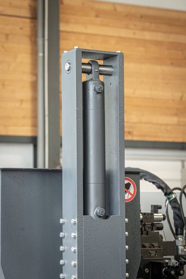 A gray filling tower with a cylinder hanging downwards on a briquetting press