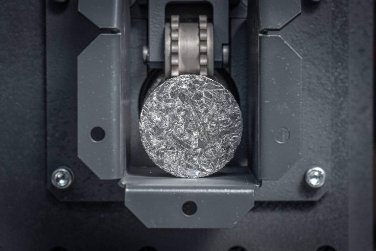 A round metal briquette in the discharge of a briquetting press