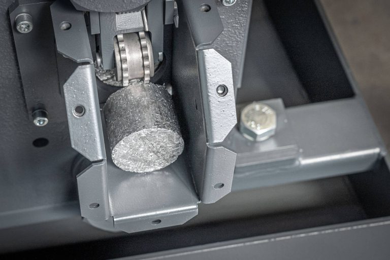 A round metal briquette in the discharge of a briquetting press