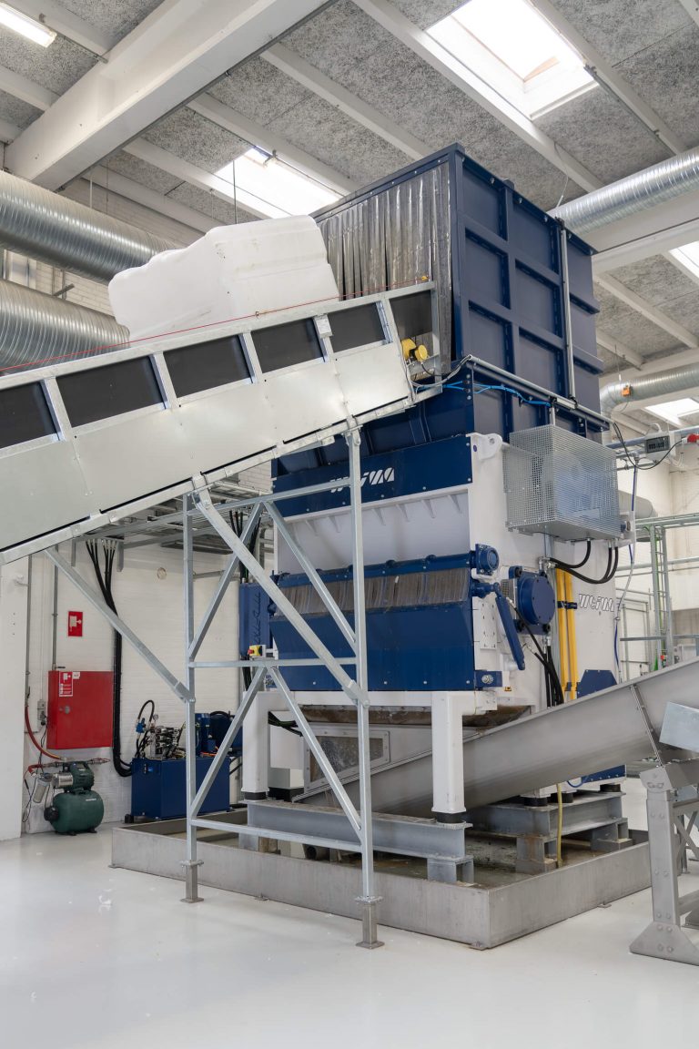 Ein IBC Container wird über ein Förderband in einen Shredder von WEIMA transportiert.