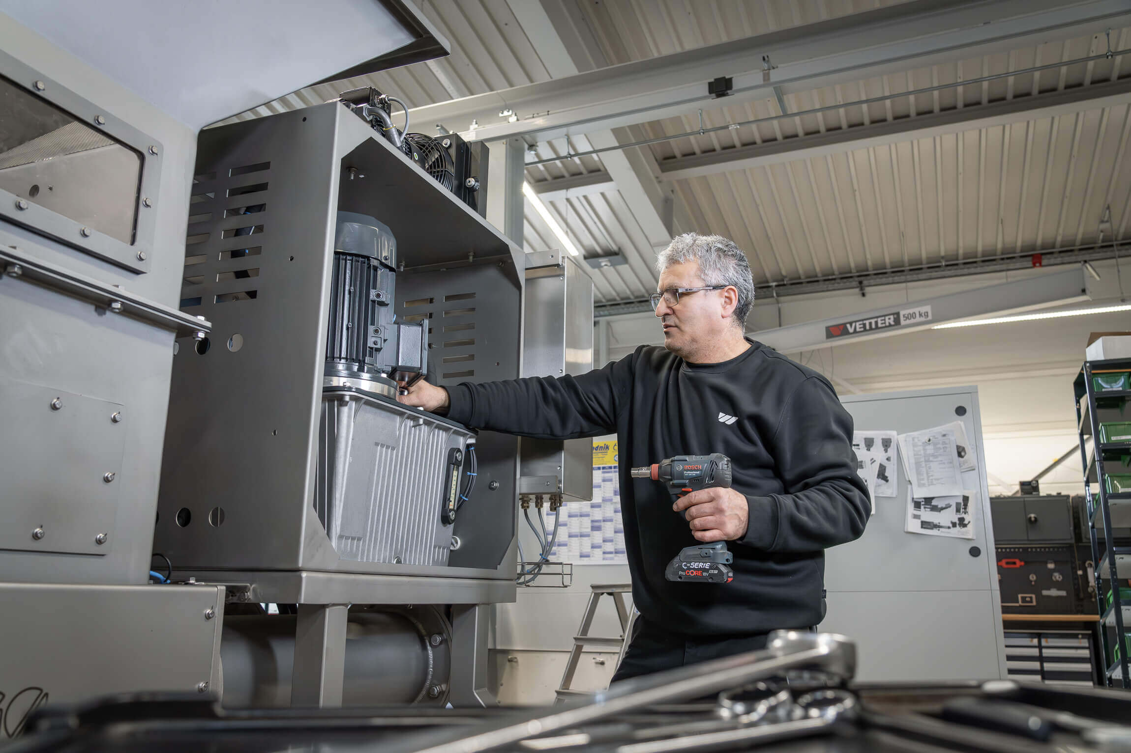 Mann mit Akkuschrauber in der Hand an einer silbernen Entwässerungspresse