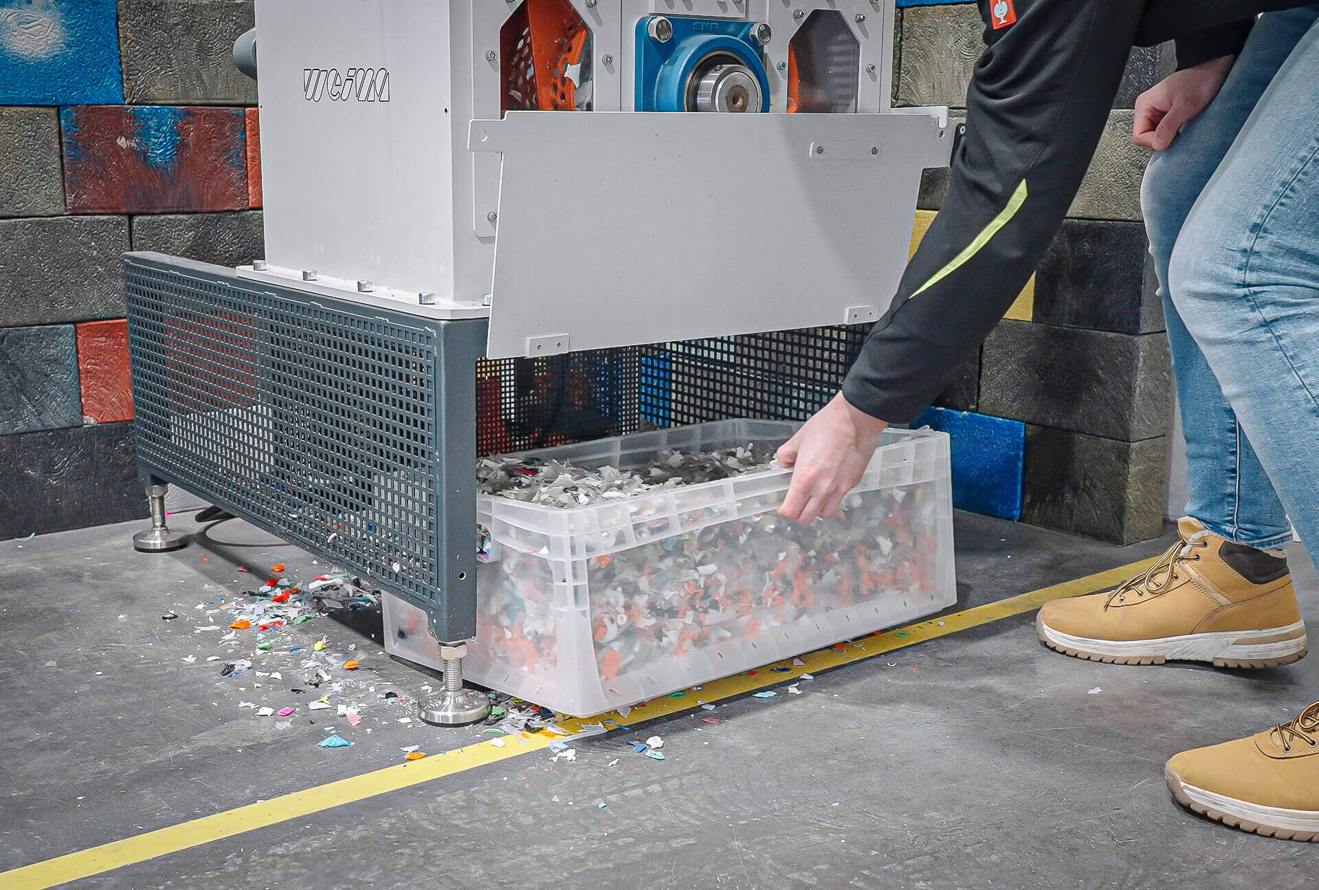 Post-consumer packaging shredded to 15 mm plastic flakes inside a box underneath a shredder