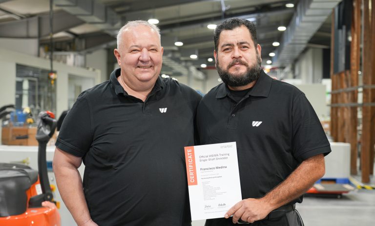 Zwei in schwarzem T- Shirt gekleidete Männern stehen nebeneinander lachend, der eine mit einem Trainingszertifikat von WEIMA