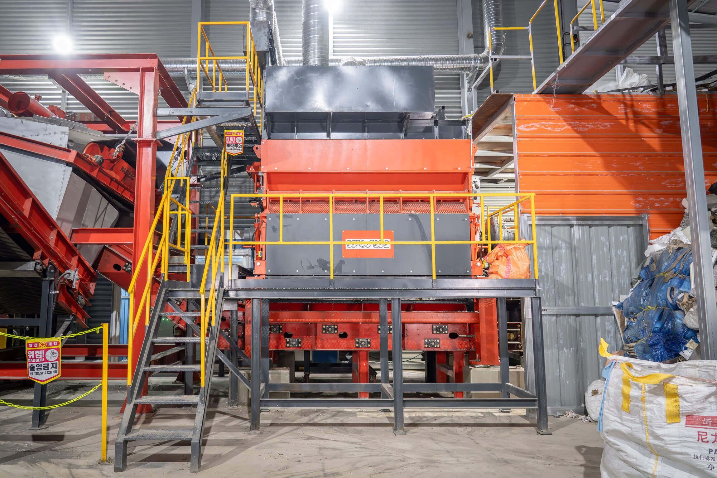 orange shredder installed in a warehouse between a crane for filling and a magnetic belt