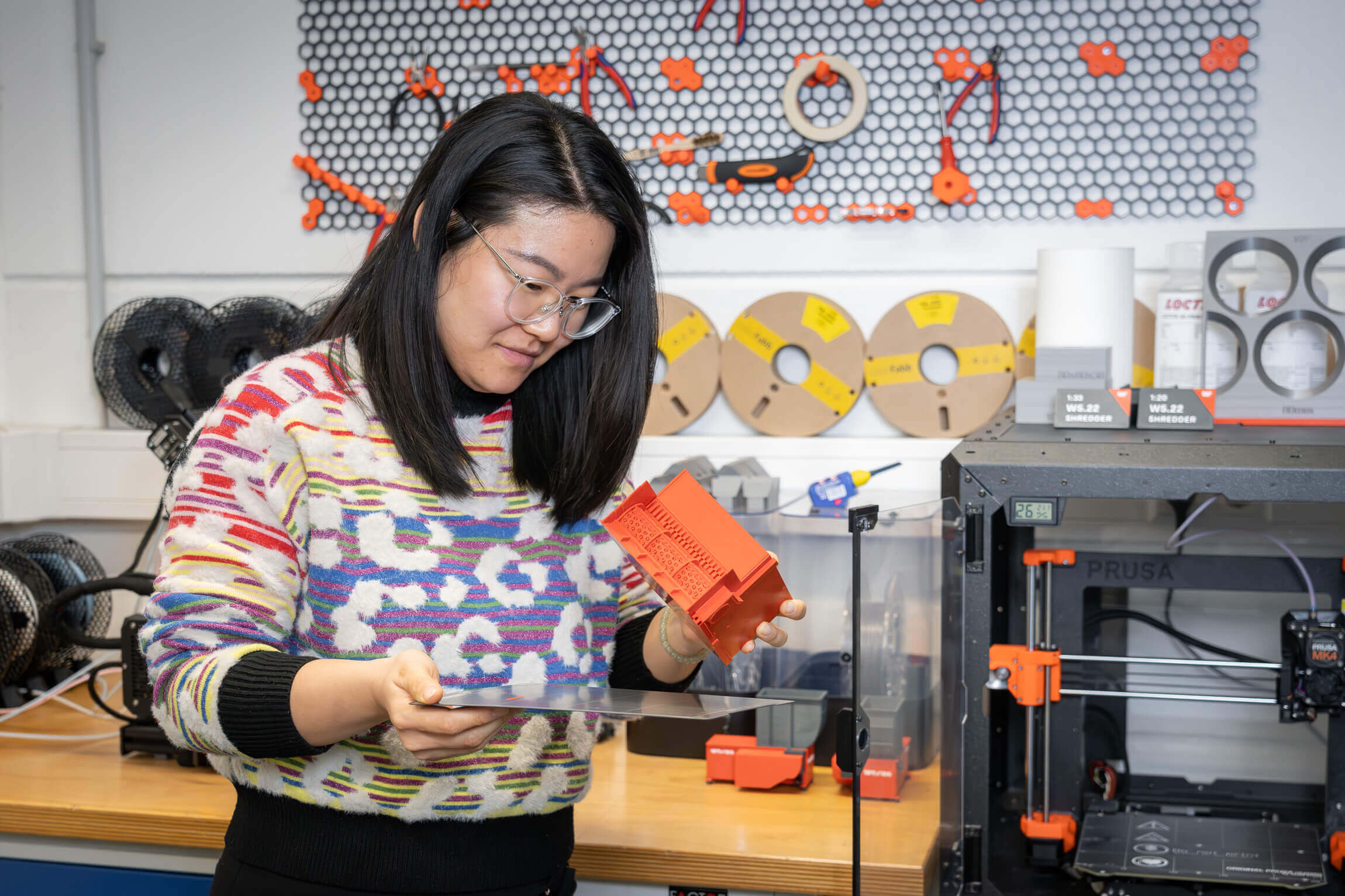 Frau schaut auf ein 3D-Druck Modell in ihrer Hand in einer 3D-Druck Werkstatt