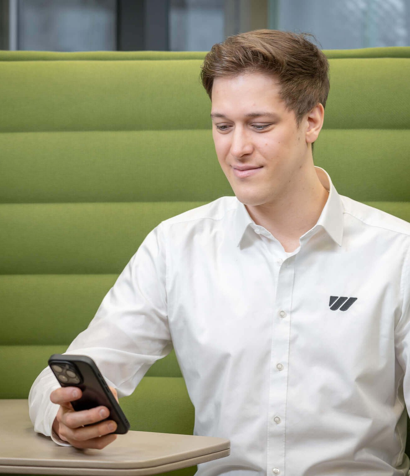 Mann in weißem Hemd sitzt in einem grünen Sessel und schaut auf sein Handy