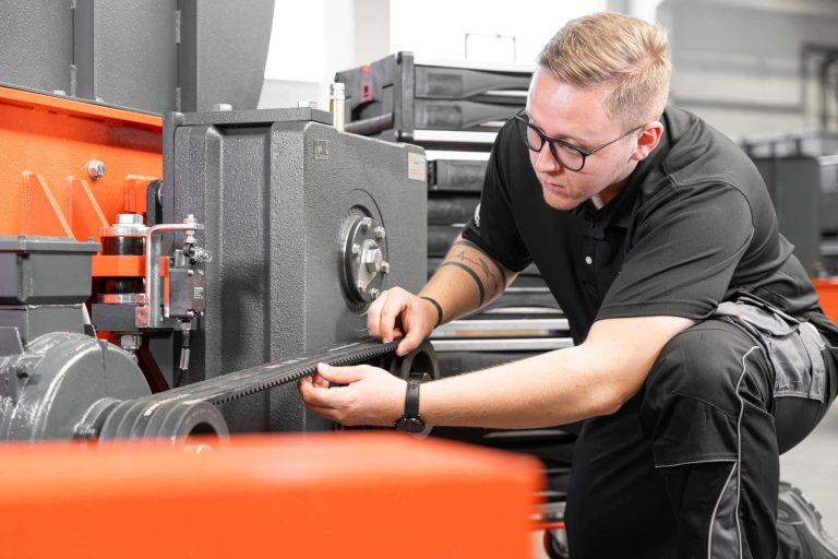 WEIMA employee with black shirt inspecting drive unit of an orange WEIMA shredder