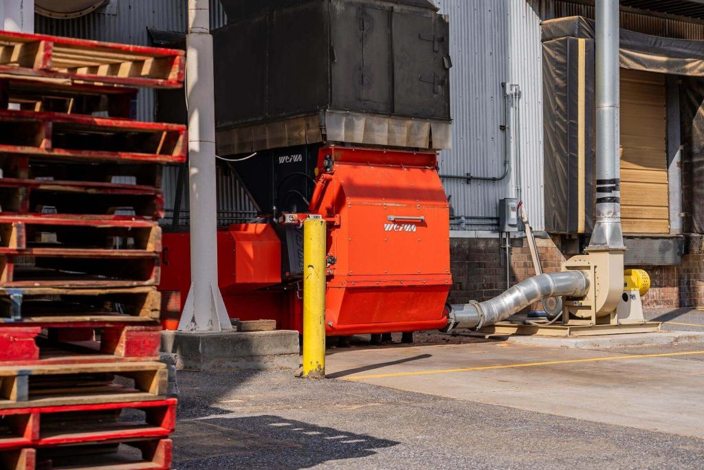 An orange WEIMA WLK 13 single-shaft shredder sits behind a warehouse.