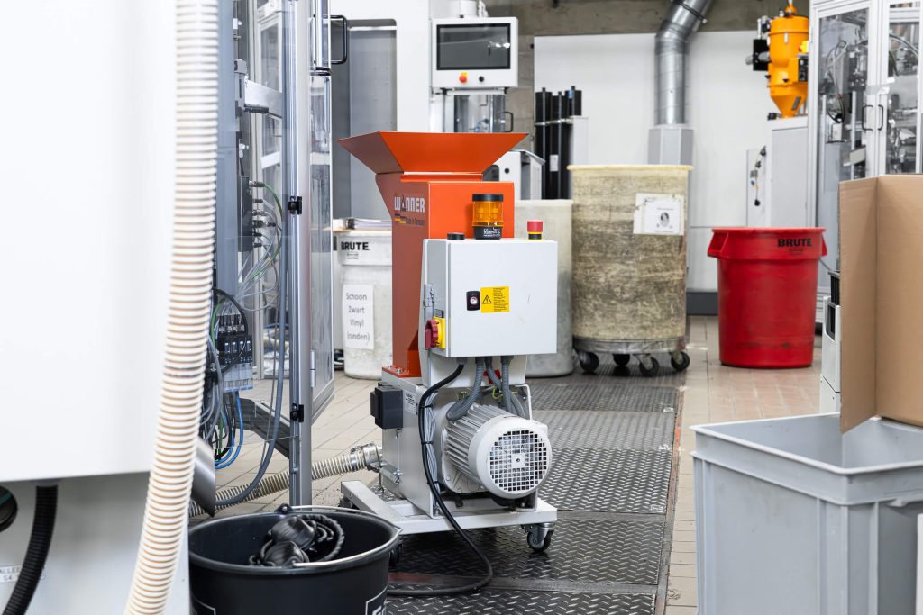 Rückansicht einer Wanner C-Serie Schneidmühle neben einer Pressmaschine zur Schallplatten Produktion