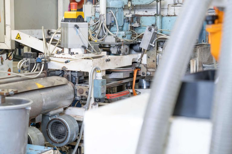 Detailaufnahme einer Schallplatten Pressmaschine, dabei ist das Abtrennen eines orangenen PVC Überstands sichtbar