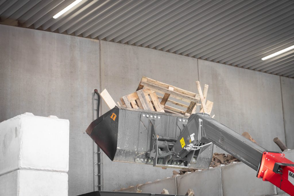 Wooden pallets and coarse wood scrap are transported by the telehandler into the feed hopper of the WEIMA shredder – ready for further processing.