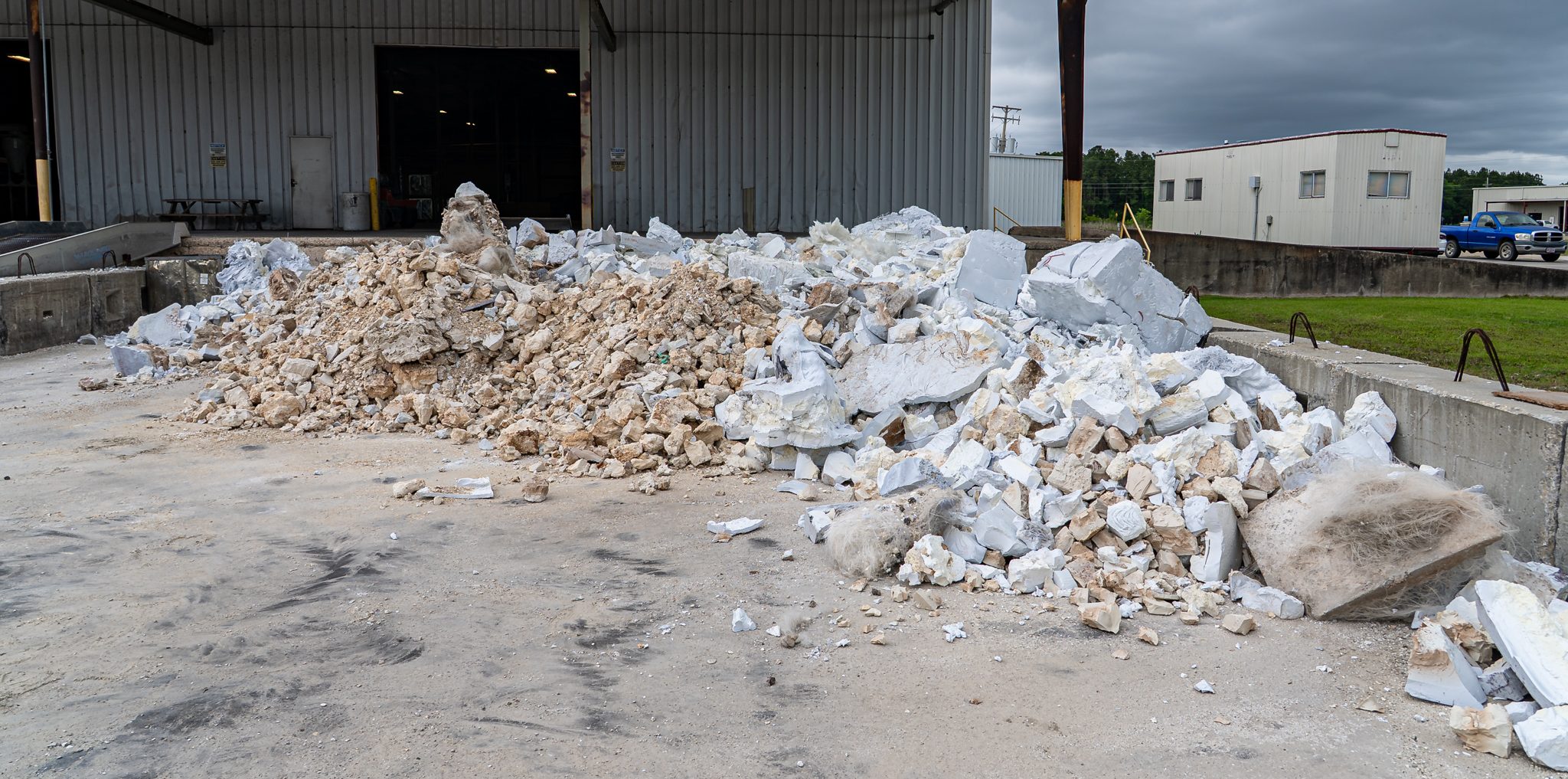 Pile of plastic and foam waste in front of an industrial hall.