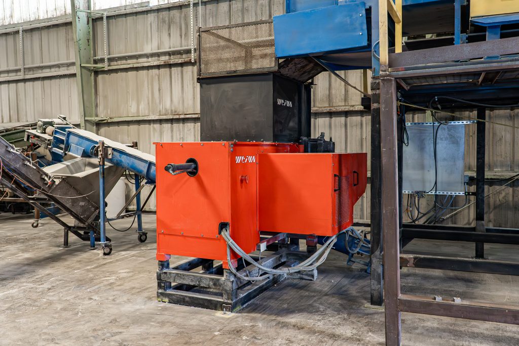 A red WEIMA shredder with an attached conveyor belt is ready for material processing in a workshop.
