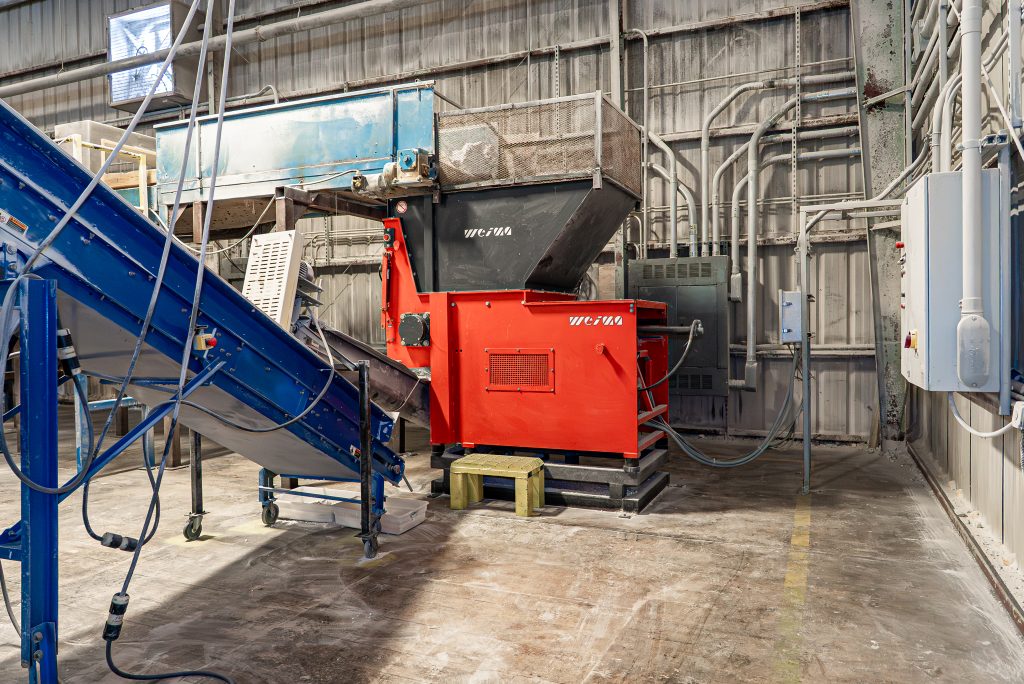 A red WEIMA shredder with an attached conveyor belt is ready for material processing in a workshop.