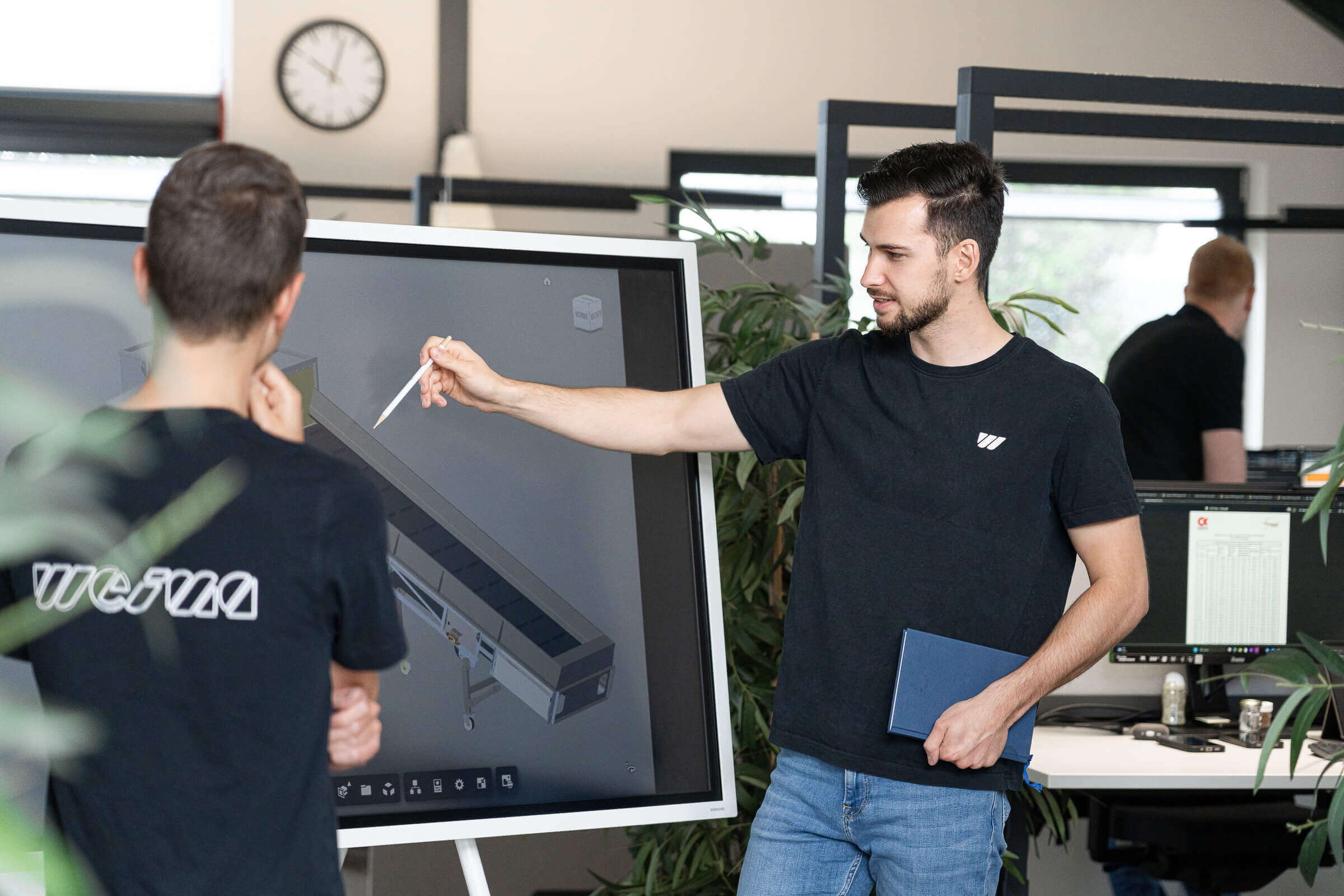 Zwei WEIMA Service Mitarbeiter stehen vor einem Touchscreen und besprechen ein Projekt im Büro