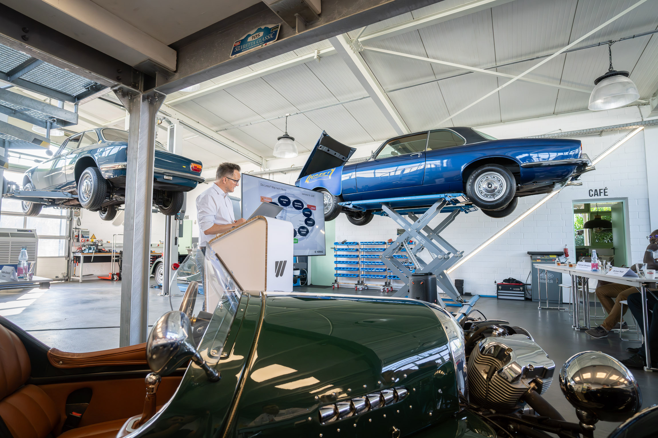 A man gives a lecture on neuromarketing, standing in the middle of old vintage cars from the WEIMA garage